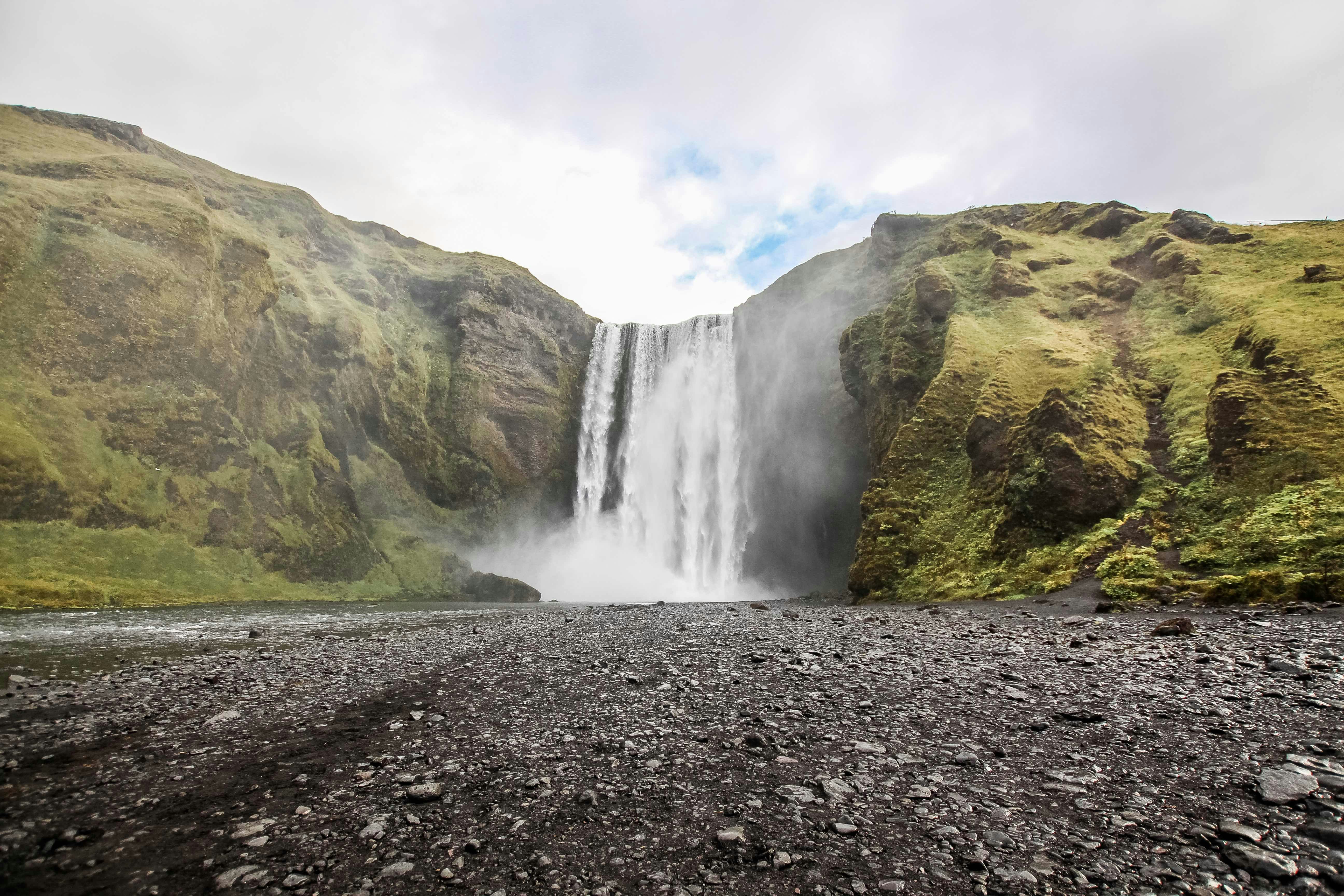 photo of waterfall near mountain under blue sky at daytime